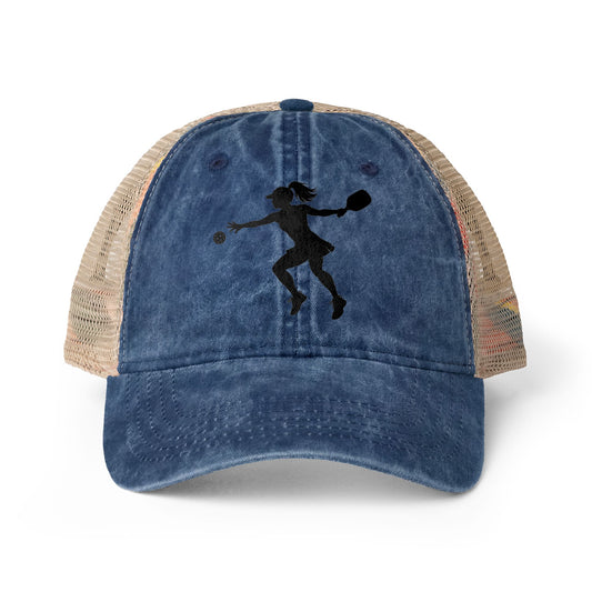 A distressed blue trucker hat with beige mesh side panels featuring a black silhouette graphic of a female pickleball player on the front, shown on a white background.